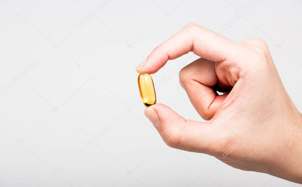 Yellow Omega 3 capsule squeezed in fingers on white background
