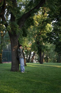 A man stands by a tree and talks on the phone