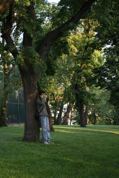 A man stands by a tree and talks on the phone