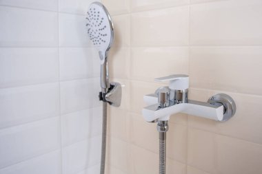 Sıcak ve soğuk su için musluk, duş hortumuyla banyodaki bir duvara monte edilmiş. Modern bir banyo.