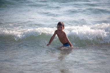 Sahilde küçük bir çocuk, yaz zamanı dalgalarla oynuyor. Rahatlama ve sağlıklı bir yaşam tarzı. Yaz tatili, sağlık gelişimi