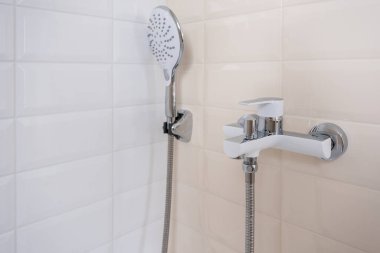 Sıcak ve soğuk su için musluk, duş hortumuyla banyodaki bir duvara monte edilmiş. Modern bir banyo.