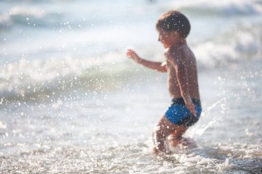 Sahilde küçük bir çocuk, yaz zamanı dalgalarla oynuyor. Rahatlama ve sağlıklı yaşam tarzı kavramı