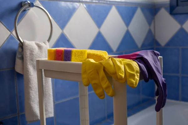 Rubber gloves and sponges on white shelf inside bathroom. Closeup. Set of colorful accessory for house cleaning. Clean house. Front view.