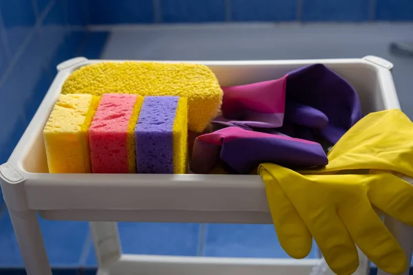 Rubber gloves and sponges on white shelf inside bathroom. Closeup. Set of colorful accessory for house cleaning. Clean house. Front view.