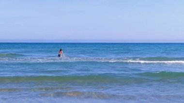 A boy entering  the sea, view from the back. Blue sea and sandy beach. Mediterranean coast. Healthy lifestyle, vacation, summer holidays
