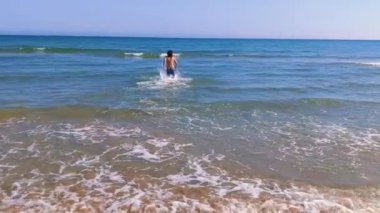 A boy entering  the sea, view from the back. Blue sea and sandy beach. Mediterranean coast. Healthy lifestyle, vacation, summer holidays