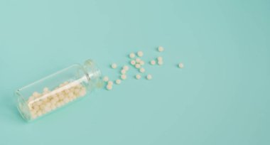 Alternative homeopathy medicine concept. Homeopathic globules scattered from a clear glass bottle on light blue background, copyspace for text. Healtcare and pills concept