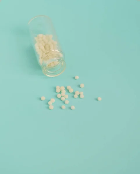 Alternative homeopathy medicine concept. Homeopathic globules scattered from a clear glass bottle on light blue background, copyspace for text. Healtcare and pills concept