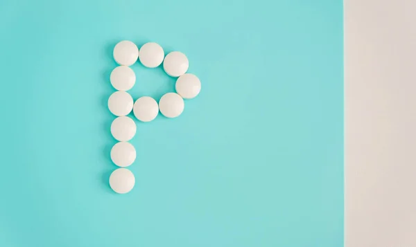 Letter P made from white pills on a blue background. White medical pills. Macro top view with copy space. Health care and pills concept, pharmaceutical, disease prevention