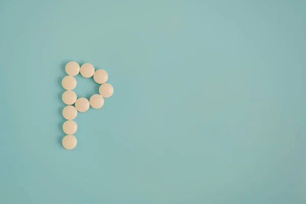 Letter P made from white pills on a blue background. White medical pills. Macro top view with copy space. Health care and pills concept, pharmaceutical, disease prevention