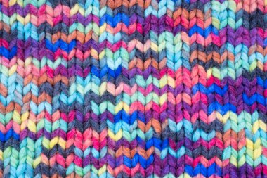 Woolen knitted background with a relief pattern. The texture of the fabric of a blanket or scarf is large. Wool, manual typewriter, handmade. Wildly Variegateds color. Knitted fabric as background