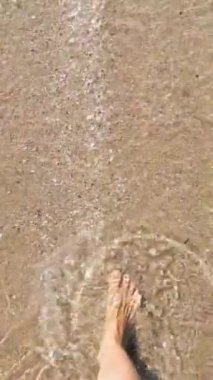 Woman feet walking along sea water waves on sandy beach. Female on summer travel vacation, slow motion. Sitges beach on a sunny day, Barcelona, Spain. Concept of summer vacation