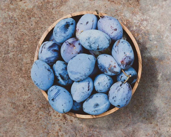 Purple fruits of a Stanley prune plum. Plum fruits variety Stanley. Ripe plums in a wooden bowl. Concept of home gardening and harvesting