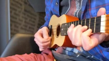 Adam ukulele çalıyor, ağır çekimde. Adam tellere dokunuyor. Enstrümanlı bir müzisyen. Erkek çalıyor, şarkı söylüyor, tatilin tadını çıkarıyor, seyahat ediyor. Ahşap ukulele