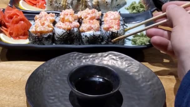 寿司ロール 黒皿に盛り付けた寿司の種類も豊富 箸で黒スレートの板から寿司ロールを1つ取り 閉じます 日本料理を食べるという概念 — ストック動画