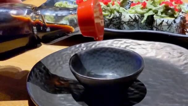寿司卷 在黑盘上的寿司种类繁多 将酱油倒入木桌上的一小碗黑酱汁中 — 图库视频影像