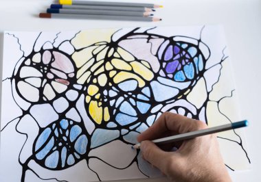 A woman draws a neurographic drawing on paper with color pencils. Neurographic art is an easy way to work with the subconscious mind through drawing. Taking care of yourself