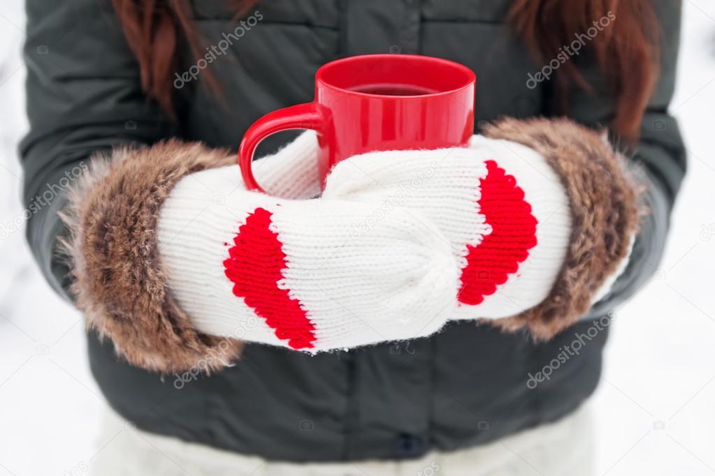 Hands in mittens with hearts holding cup