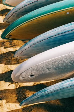 Close-up of colorful paddle boards for rent lying on the sand.