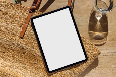 Tablet maketi, beyaz beyaz ekranlı siyah cihaz. Tahta masa üzerinde, güneş ışığı, üst görünüm.