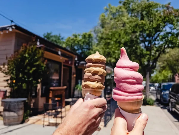 Man and woman\'s hands close-up holding fancy swirl ice-cream cones on the street