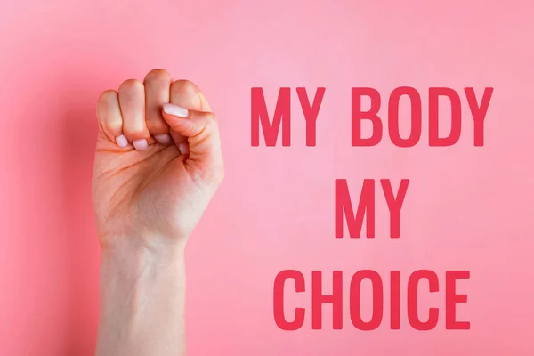 Feminine hand, raised woman fist on pink background and text My Body My Choice. Woman's rights protest concept, abortion rights.