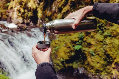 Close-up shot of man pouring hot tea from the flask outdoors