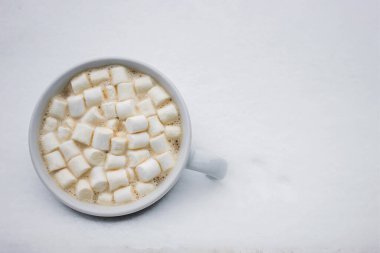 Cup with hot chocolate and marshmallow standing in the snow, top view. Winter concept.