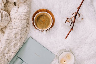 Flat lay with knitted warm sweater, candle and coffee on the bed. Winter accessories, cozy morning.