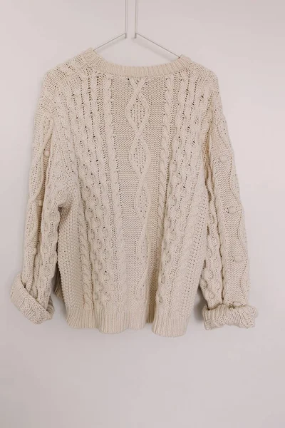 White warm woolen knitted sweater on the hanger over the white wall