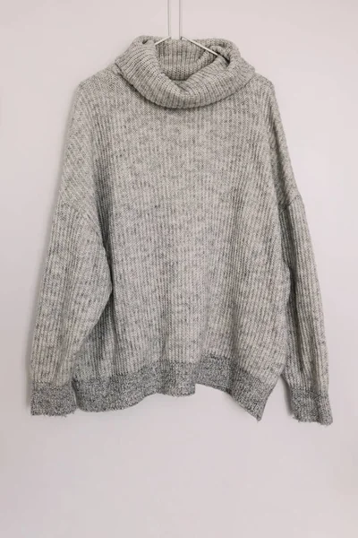 Warm woolen knitted sweater on the hanger over the white wall