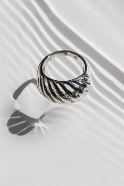 Silver ring on close-up, water ripple white background. Harsh shadows, minimalist jewelry
