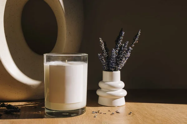 Natural wax candle with empty label and small vase with lavender flowers. Candle label mock-up. Natural sunlight, lifestyle shot
