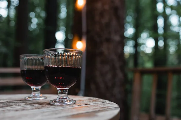 Two Glasses Red Wine Standing Wooden Table Blurred Trees Lights — 图库照片