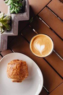 Modern kahve dükkanının masasında bir fincan sade beyaz ve çikolatalı kruvasan.