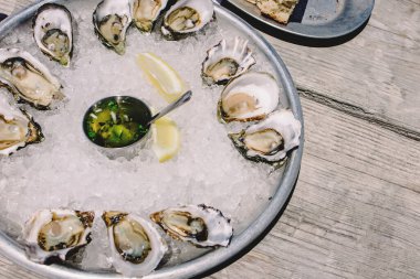 Tahta masanın üzerinde taze istiridye tepsisi ve güneş ışığı.