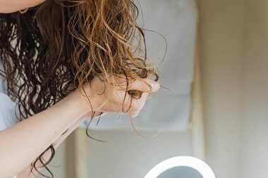 Woman scrunching her hair to form curls. Applying curly method for hair styling. Close-up on the hands clipart