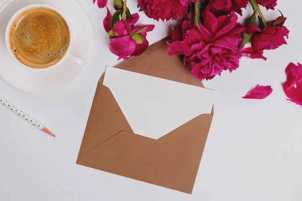 Greeting card in the envelope, flat lay with coffee and pink peonies, paper mock-up