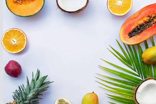 Frame with tropic fruits and palm leaf on the white background, top view