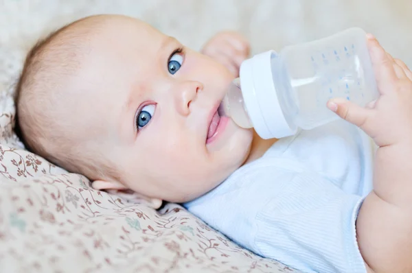 Bebé de 6 meses bebe agua de un biberón, acostado en la cama. bebe feliz y  alegre