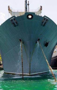 Nehir yolunda büyük bir savaş gemisinin ön görüntüsü. Siyah çapalar fiyonklardan fırlıyor..