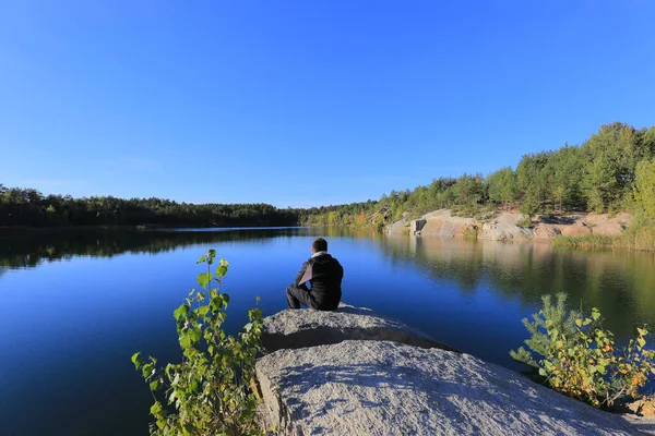 Man sits on a cliff and looks at the lake