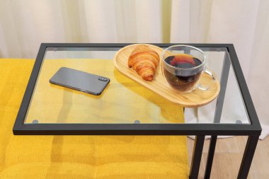 Black tea with croissant on the table near sofa