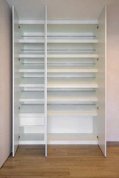 Open white wardrobe with internal shelves and in the hallway