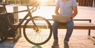 Bir süre dizüstü bilgisayarda çalışan genç adam bisikletinin yanındaki bankta oturuyor.