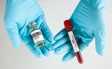 Hemşire bir elinde kovid aşı, diğer elinde de kan tüpü tutuyor. Aşı olun ya da her seferinde koronavirüs testi yapın.