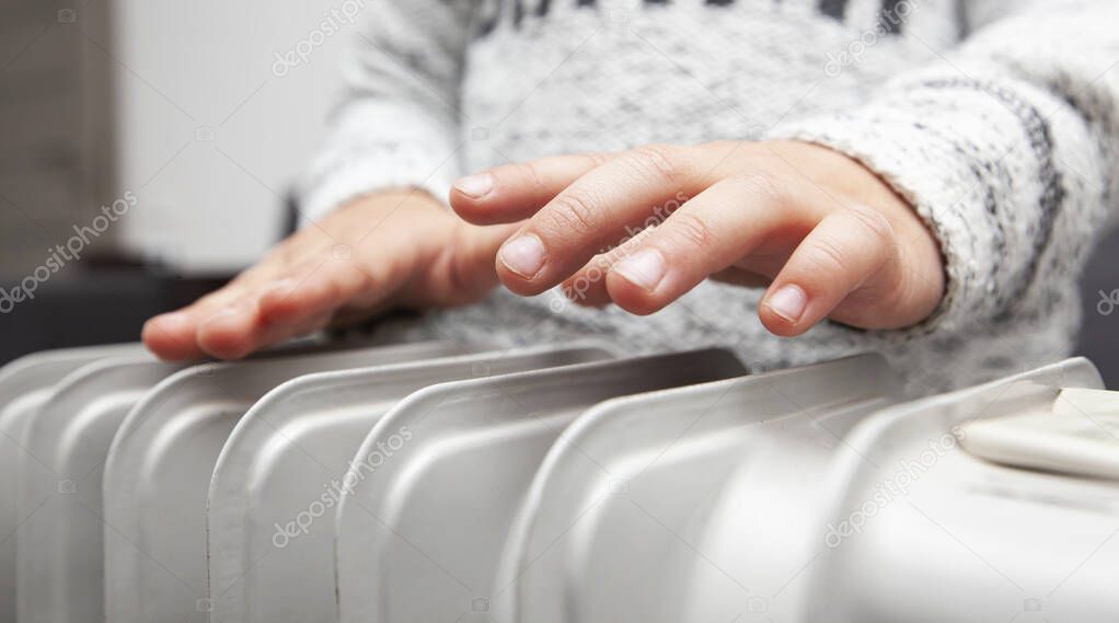 Boy warms hands above the electric oil radiator