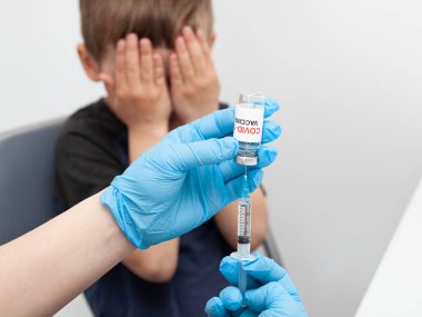 Çocuk iğneden korkuyor. Çocuk aşıdan korktuğu için elleriyle yüzünü kapadı.