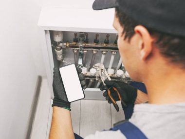 Su tesisatçısının elinde koruyucu eldivenli beyaz ekran cep telefonu.